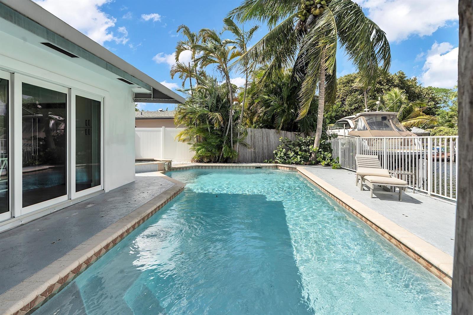 A swimming pool sits beside a white house with sliding glass doors and palm trees — 2233 SE 15th Street, Pompano Beach FL 33062, POMPANO BEACH, FL