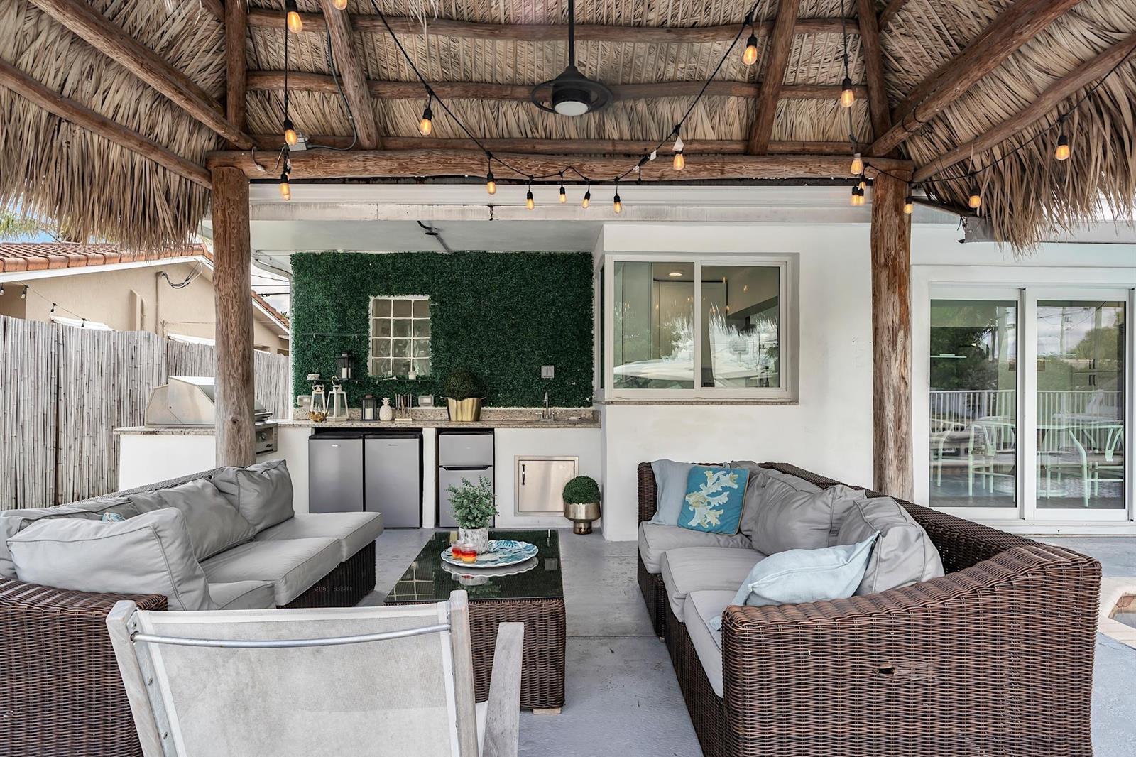 An outdoor patio features a thatched roof, wicker seating, a kitchen area, and string lights — 2233 SE 15th Street, Pompano Beach FL 33062, POMPANO BEACH, FL