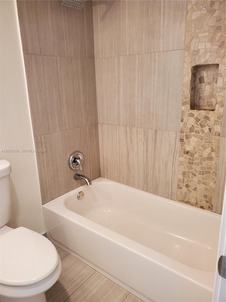 A bathroom features a white bathtub, a toilet, and light-colored tile walls with a mosaic niche — 1230 NE 139th St # 409, North Miami FL 33161, NORTH MIAMI, FL