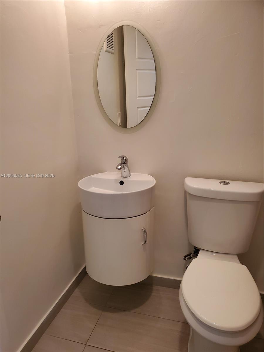 A small bathroom features a white pedestal sink, a toilet, and an oval wall mirror — 1230 NE 139th St # 409, North Miami FL 33161, NORTH MIAMI, FL