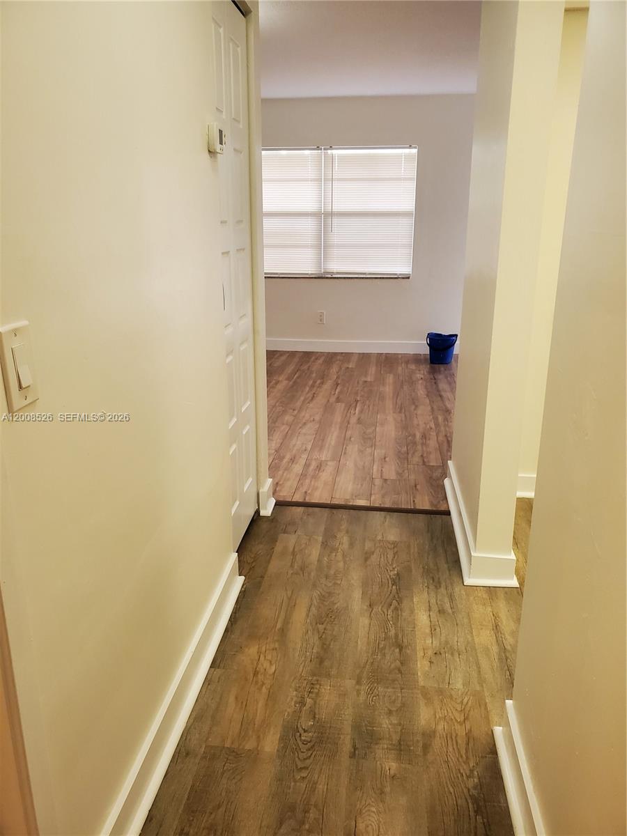 A hallway with wood-look flooring leads into a room with a window and blinds — 1230 NE 139th St # 409, North Miami FL 33161, NORTH MIAMI, FL