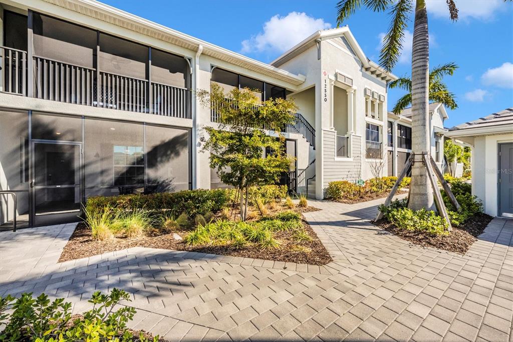 A multi-story residential building with screened balconies and a paved walkway in the foreground — 12550 GALAPAGOS STREET UNIT 104, VENICE, FL