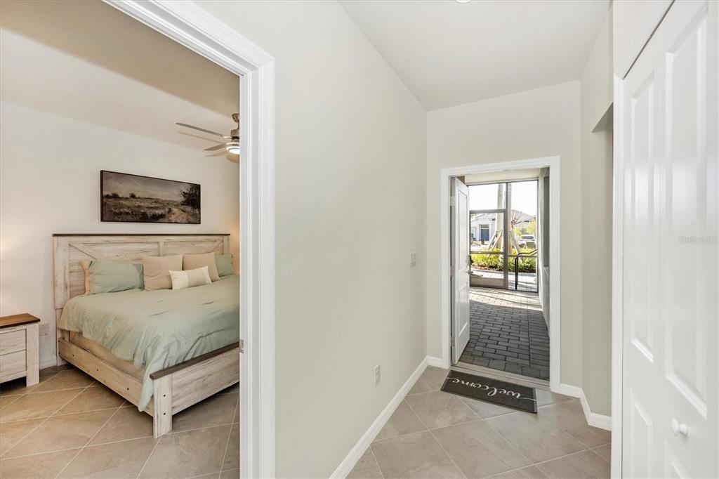 A bedroom with a rustic headboard is visible through a doorway next to an entryway — 12550 GALAPAGOS STREET UNIT 104, VENICE, FL
