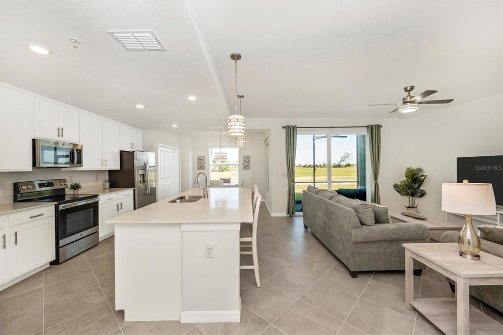 An open-concept kitchen and living area features white cabinetry, a central island, and tile flooring — 12550 GALAPAGOS STREET UNIT 104, VENICE, FL