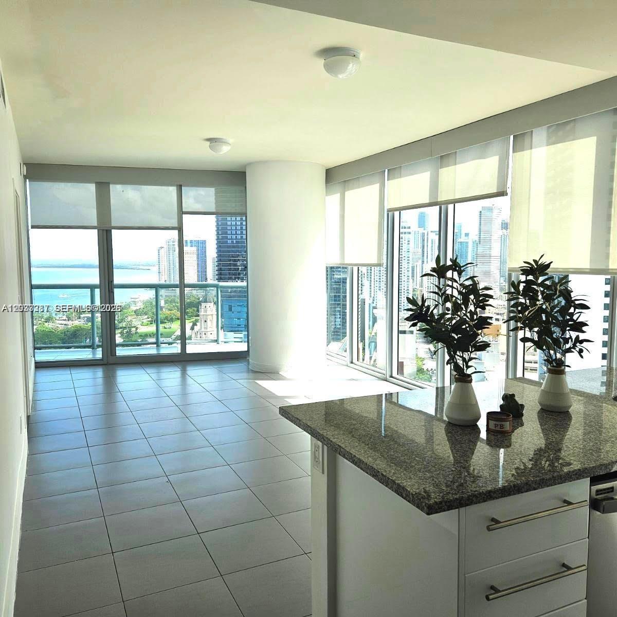 A bright kitchen island with granite countertops overlooks a living area with floor-to-ceiling windows — 888 Biscayne Blvd # 3001, Miami FL 33132, MIAMI, FL