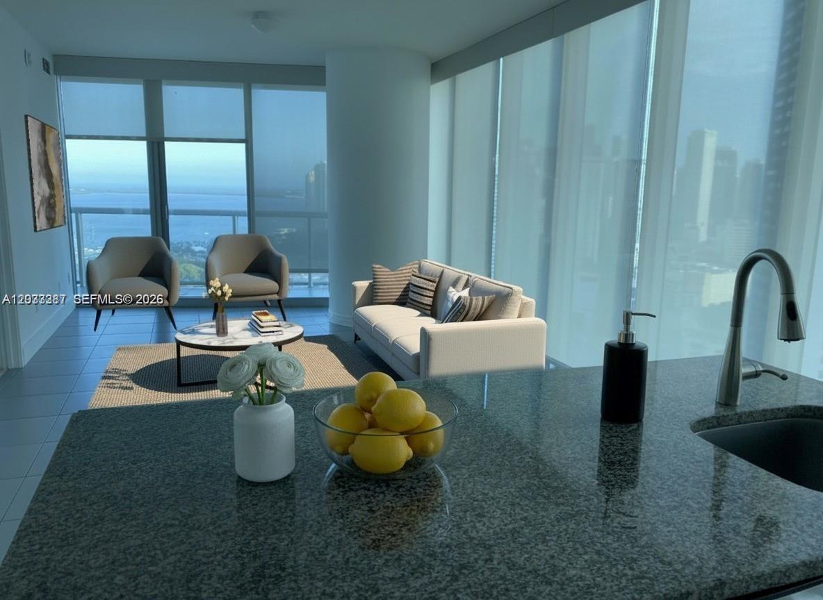 A kitchen island with a bowl of lemons overlooks a living area with floor-to-ceiling windows — 888 Biscayne Blvd # 3001, Miami FL 33132, MIAMI, FL