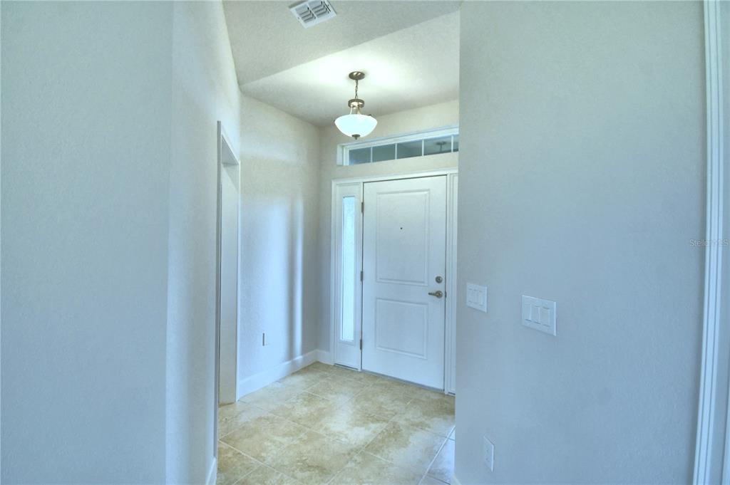 A bright entryway features a white front door, tile flooring, and a hanging light fixture — 4624 CALAMINT LANE, AUBURNDALE, FL