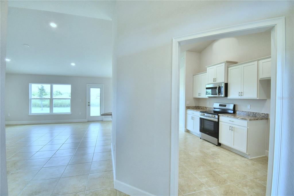 A view from a tiled hallway into a kitchen with white cabinets and an adjacent living area — 4624 CALAMINT LANE, AUBURNDALE, FL