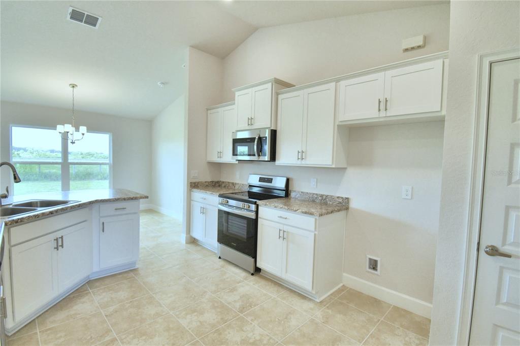 A kitchen features white cabinets, granite countertops, stainless steel appliances, and tile flooring — 4624 CALAMINT LANE, AUBURNDALE, FL