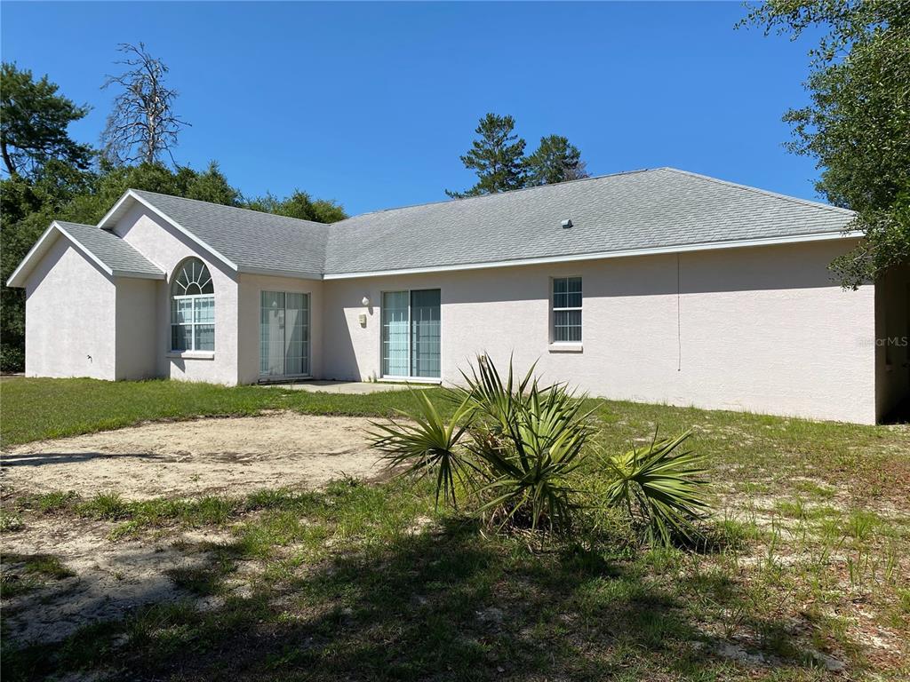 The rear exterior of a single-story stucco house features a patio and sliding glass doors — 15980 SW 27TH AVENUE ROAD, OCALA, FL