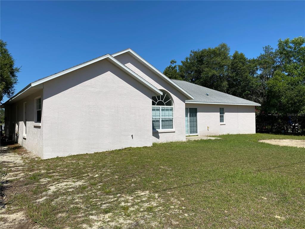 The exterior of a light-colored stucco house features a large arched window and sliding doors — 15980 SW 27TH AVENUE ROAD, OCALA, FL