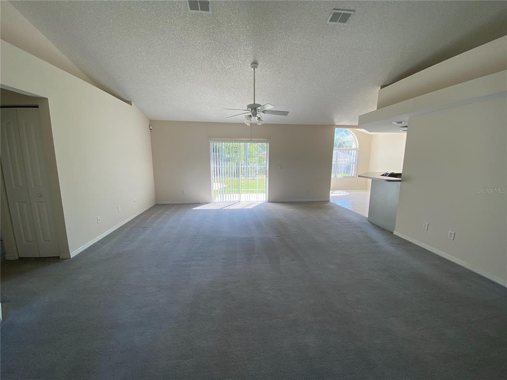A spacious living room features gray carpeting, a ceiling fan, and sliding glass doors — 15980 SW 27TH AVENUE ROAD, OCALA, FL