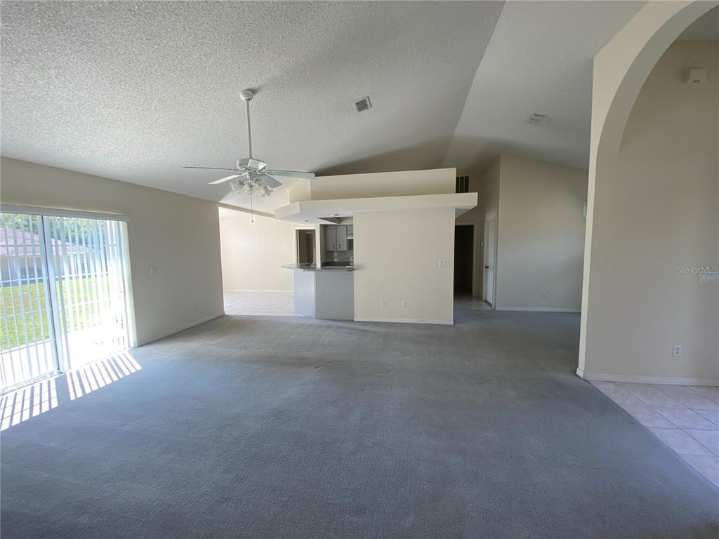 A spacious living room with gray carpeting, a ceiling fan, and an open kitchen area — 15980 SW 27TH AVENUE ROAD, OCALA, FL