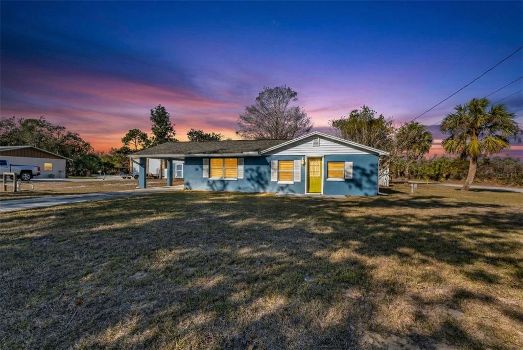 A blue single-story house with a carport and a yellow front door at sunset — 3215 PARK DRIVE, PUNTA GORDA, FL