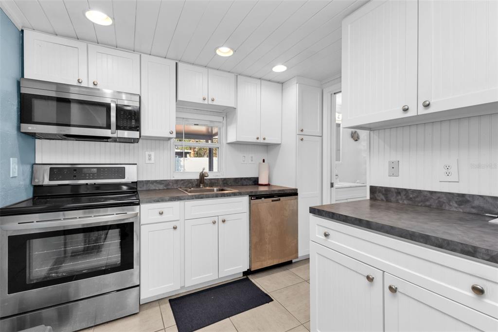 A kitchen featuring white cabinets, stainless steel appliances, dark countertops, and a beadboard ceiling — 3215 PARK DRIVE, PUNTA GORDA, FL