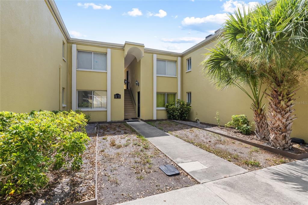 The exterior of a two-story yellow apartment building features a central walkway and palm trees — 3206 W AZEELE STREET UNIT 227, TAMPA, FL