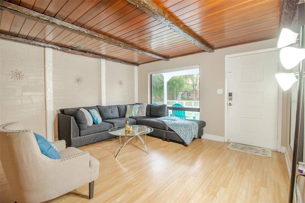 A living room features a wood-paneled ceiling, light wood flooring, a grey sectional, and a beige armchair — 1245 CATALPA LN UNIT 2, ORLANDO, FL