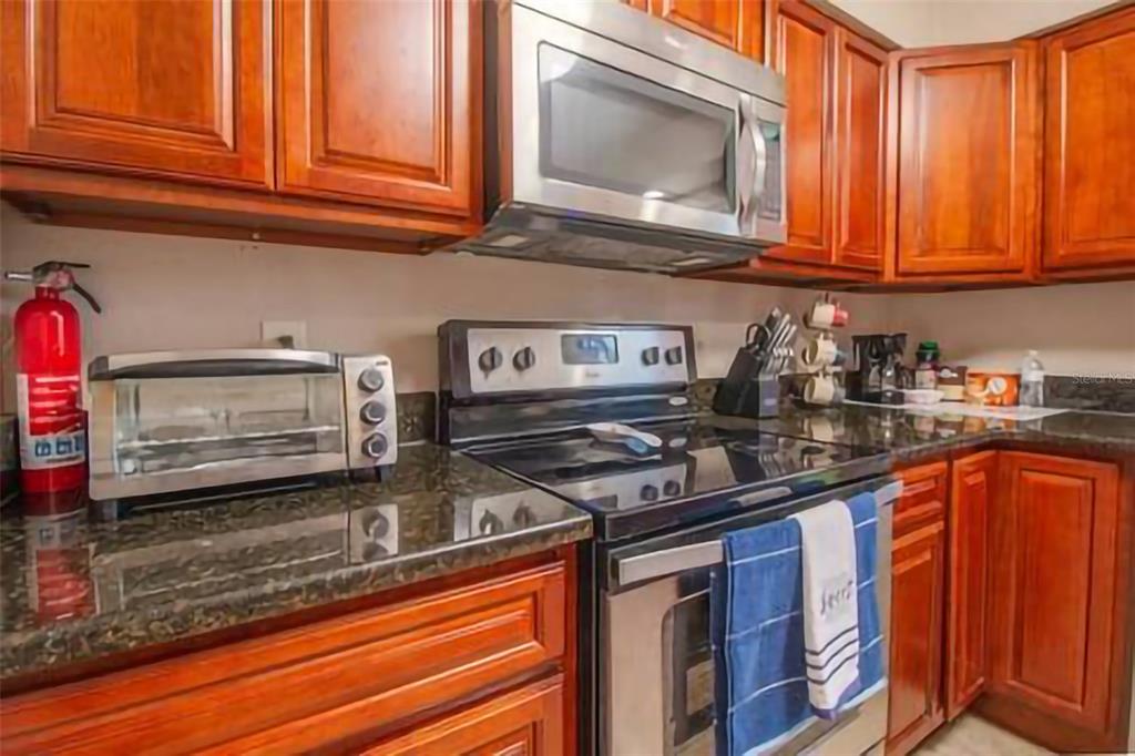 A kitchen features wood cabinets, stainless steel appliances, and dark granite countertops — 1245 CATALPA LN UNIT 2, ORLANDO, FL