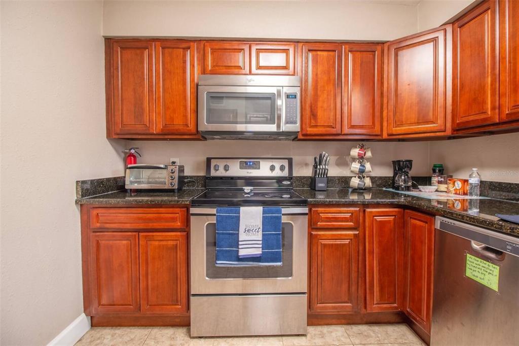 A kitchen features wood cabinets, stainless steel appliances, and dark granite countertops — 1245 CATALPA LN UNIT 2, ORLANDO, FL