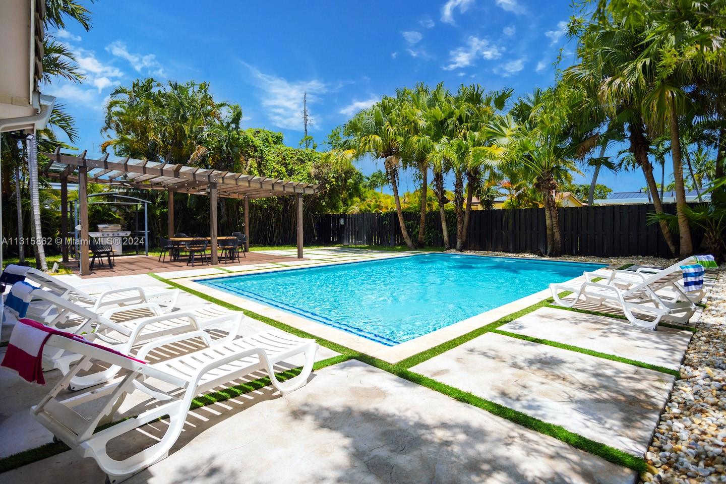 A backyard features a rectangular swimming pool, a wooden pergola, and several white lounge chairs — 1307 Rodman St, Hollywood FL 33019, HOLLYWOOD, FL