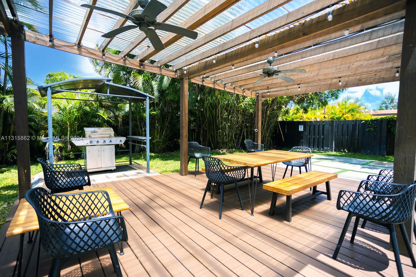 An outdoor wooden deck features a pergola, dining table with chairs, and a stainless grill — 1307 Rodman St, Hollywood FL 33019, HOLLYWOOD, FL