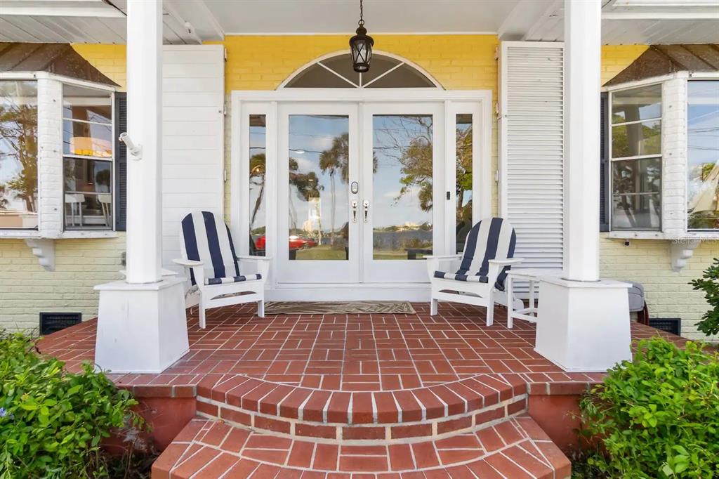 A brick porch features two striped chairs in front of white double doors and windows — 1426 RIVERSIDE DRIVE, DAYTONA BEACH, FL