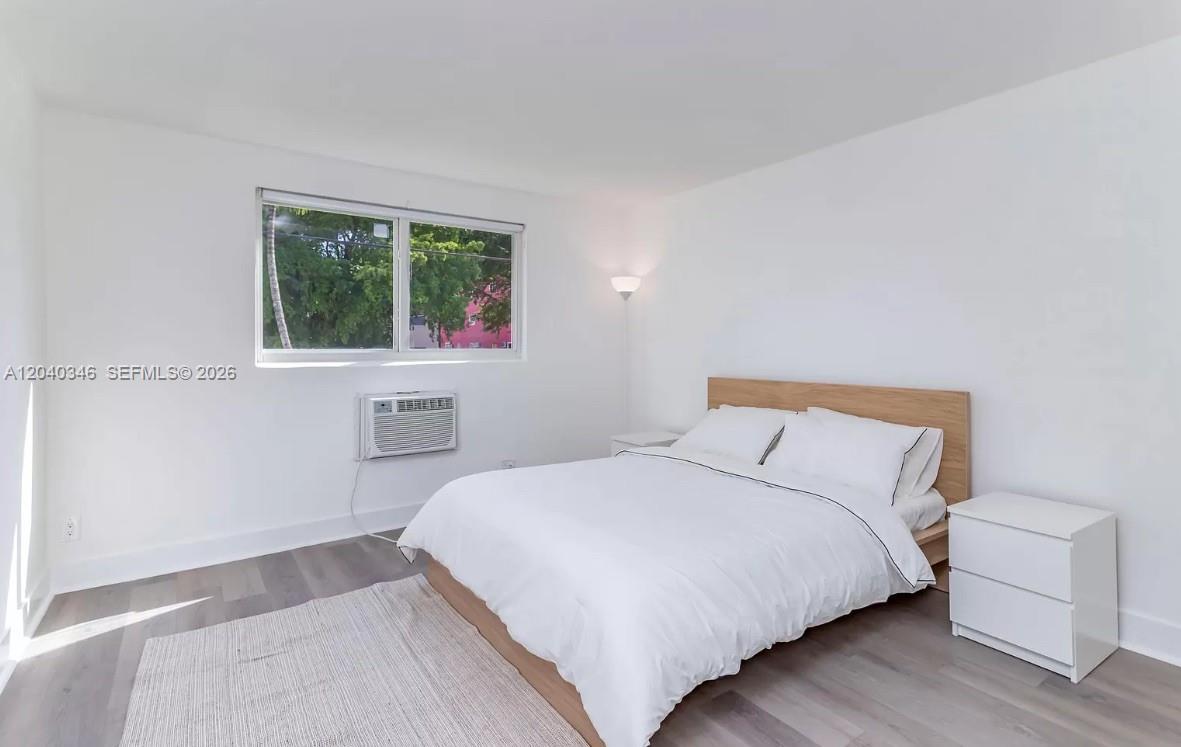 A bedroom features white walls, wood-look flooring, a bed with a wooden headboard, and a window — 143 SW 9th St # 301, Miami FL 33130, MIAMI, FL