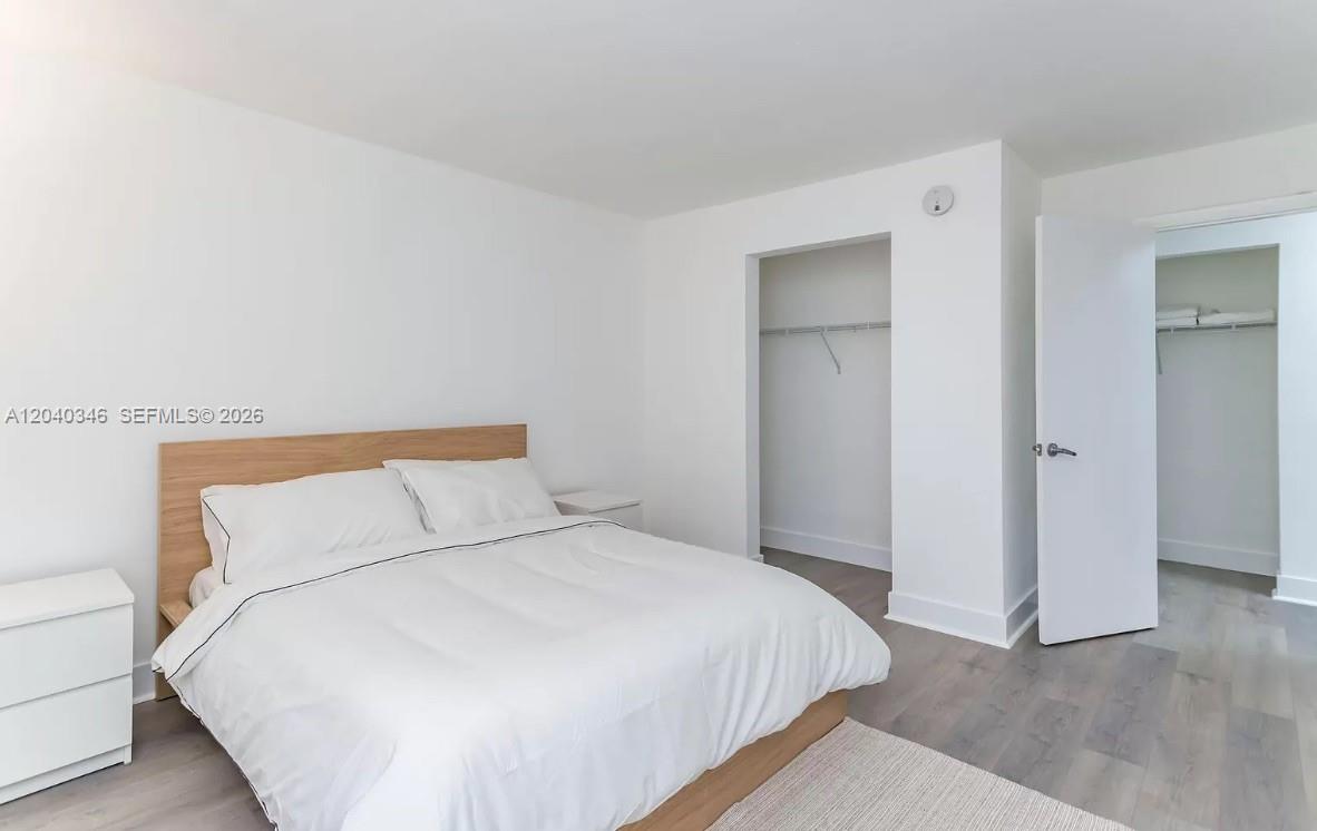 A bedroom features a wooden bed frame, white bedding, light wood flooring, and two closets — 143 SW 9th St # 301, Miami FL 33130, MIAMI, FL