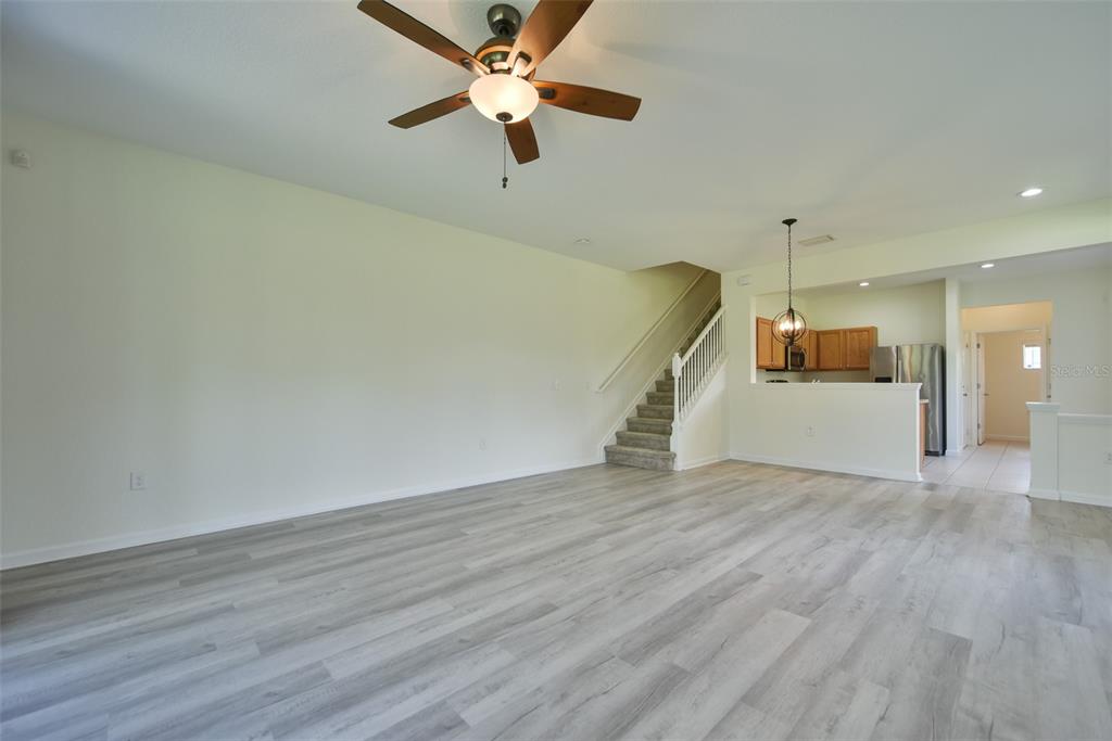 An open-concept living room features light wood-look flooring, a ceiling fan, and a staircase — 4178 SW 43RD CIRCLE, OCALA, FL