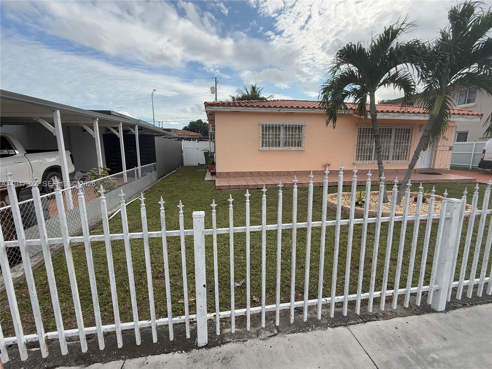 A peach-colored house with a tiled roof sits behind a white metal picket fence — 380 W 41st St, Hialeah FL 33012, HIALEAH, FL
