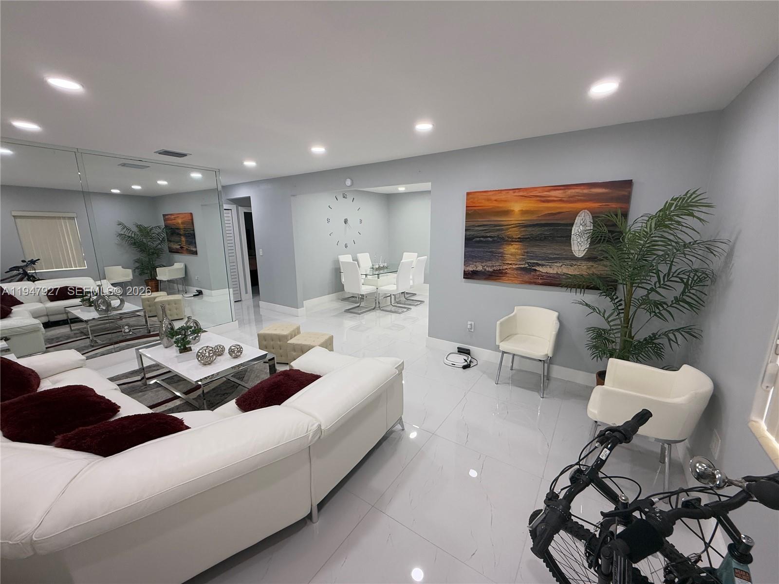 A modern living and dining area features white tile floors, a white sectional, and mirrored walls — 380 W 41st St, Hialeah FL 33012, HIALEAH, FL