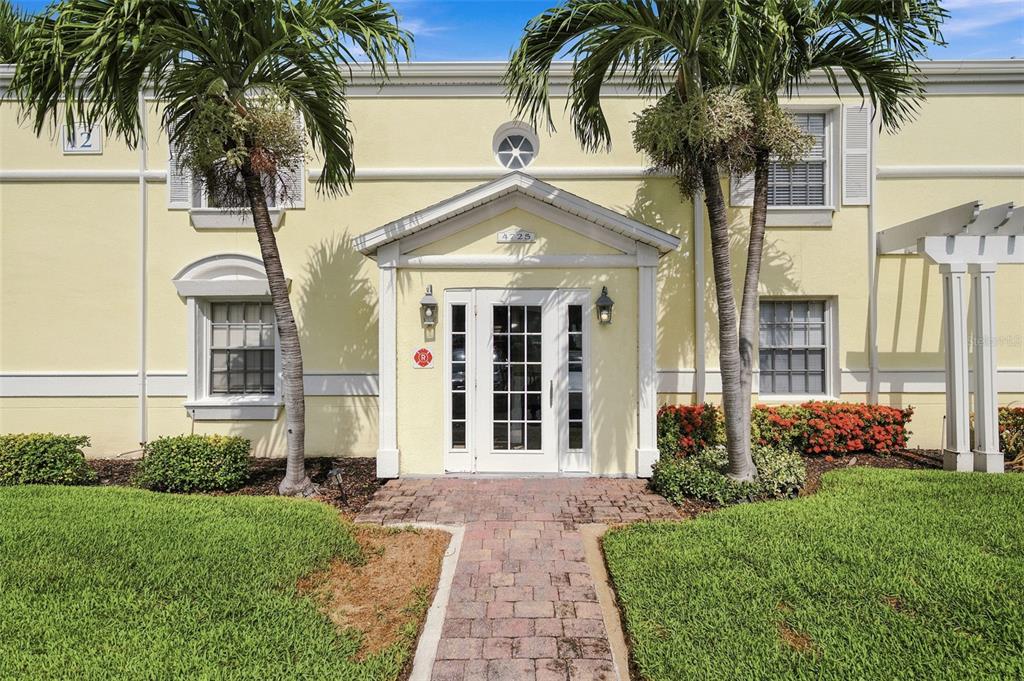A yellow two-story building features a central white-framed entrance with palm trees in front — 4725 COQUINA KEY DRIVE SE UNIT D, ST PETERSBURG, FL