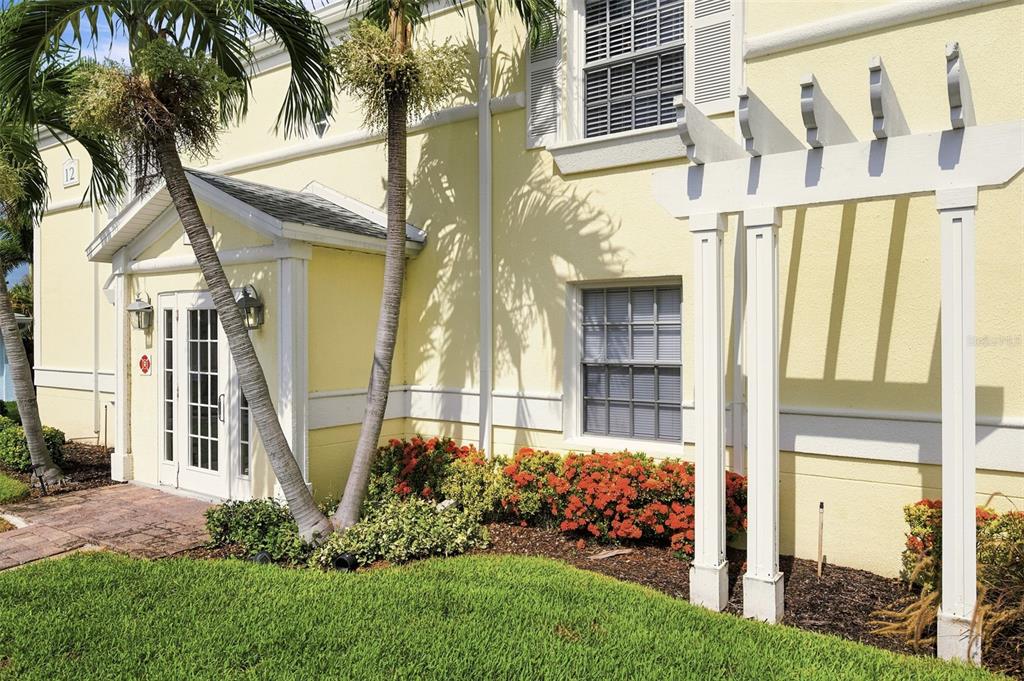 The exterior of a yellow building features a white pergola, palm trees, and landscaped bushes — 4725 COQUINA KEY DRIVE SE UNIT D, ST PETERSBURG, FL