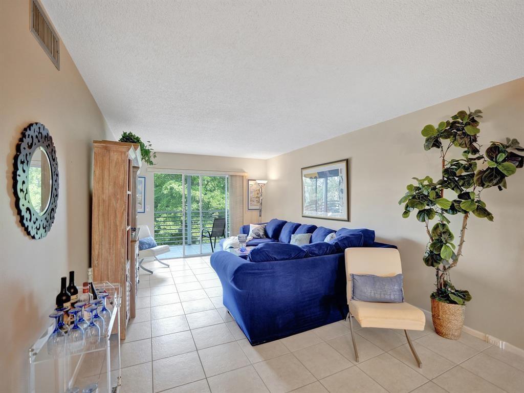 A living room features a blue sectional sofa, tile flooring, and a sliding glass door — 2003 Granada Drive # C4, Coconut Creek FL 33066, COCONUT CREEK, FL