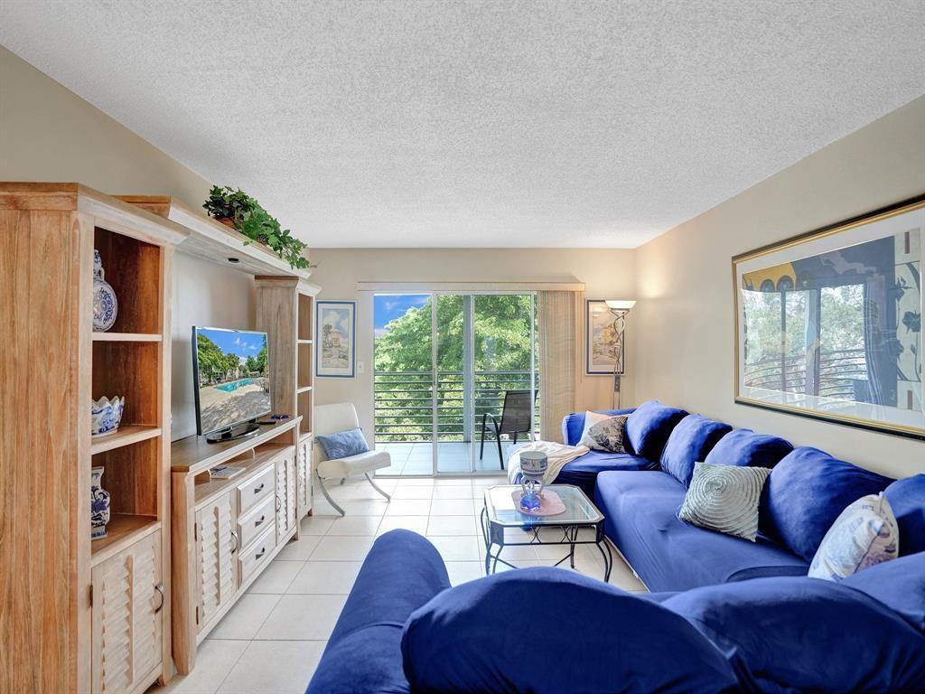 A living room features a blue sectional sofa, a wooden media console, and a balcony view — 2003 Granada Drive # C4, Coconut Creek FL 33066, COCONUT CREEK, FL