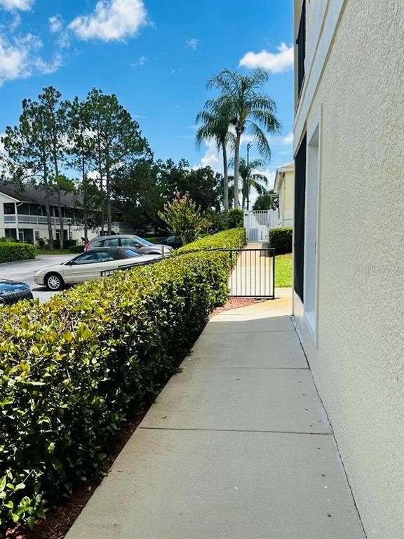 A concrete walkway runs alongside a building exterior next to a manicured hedge and parking — 8804 GRAND PALMS CIRCLE UNIT A, KISSIMMEE, FL