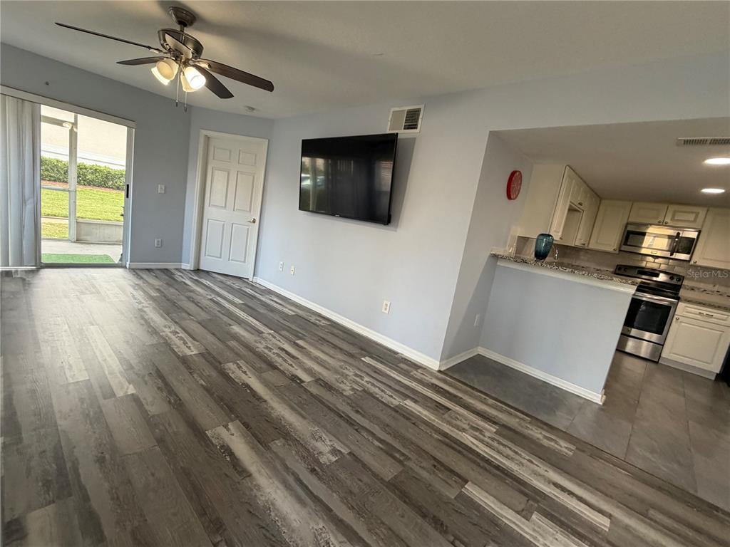A living room with wood-look flooring, a ceiling fan, and an open kitchen pass-through — 8804 GRAND PALMS CIRCLE UNIT A, KISSIMMEE, FL