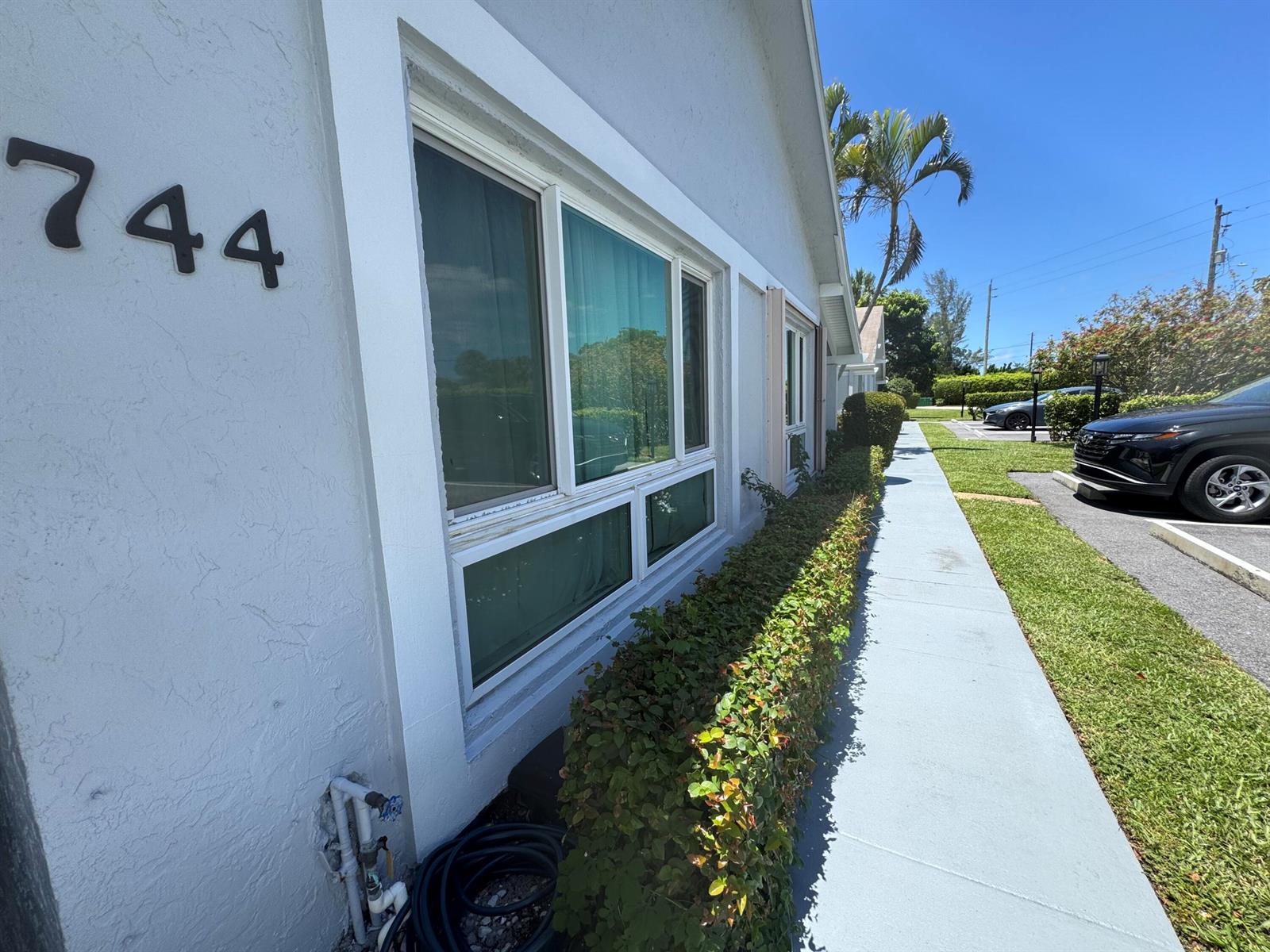 A side view of a building exterior with a hedge, sidewalk, and parked cars — 744 Lago Road # 1f, Delray Beach FL 33445, DELRAY BEACH, FL
