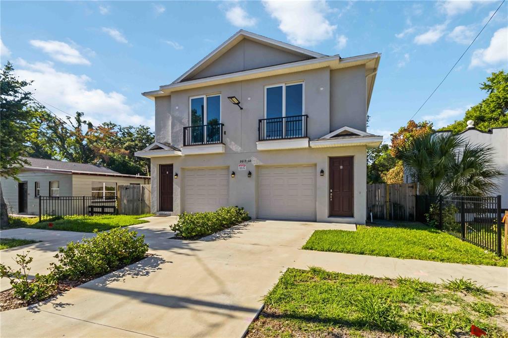 A two-story duplex features light-colored stucco siding, two garage doors, and two front entry doors — 2613 E 23RD AVENUE UNIT 1/2, TAMPA, FL