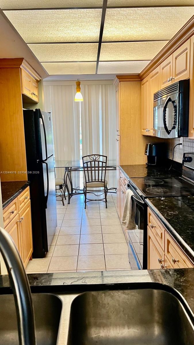 A galley kitchen features light wood cabinets, black appliances, and dark granite countertops — 8711 SW 30th St # 106, Davie FL 33328, DAVIE, FL