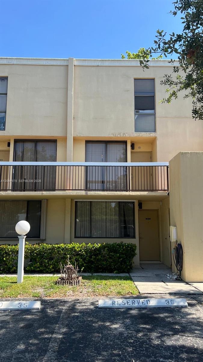 A two-story tan apartment building features a second-floor balcony and reserved parking spaces — 8711 SW 30th St # 106, Davie FL 33328, DAVIE, FL