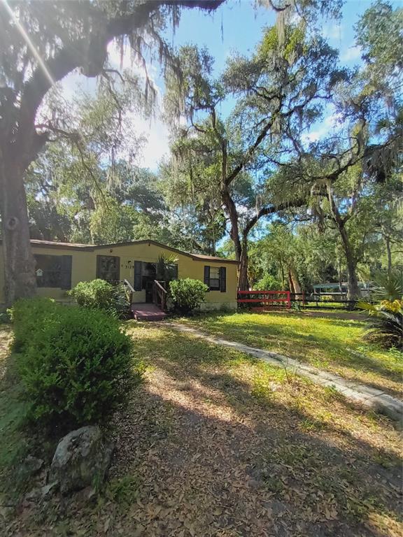 A single-story house with a tan exterior stands among large trees with hanging moss — 3128 CR 418, LAKE PANASOFFKEE, FL