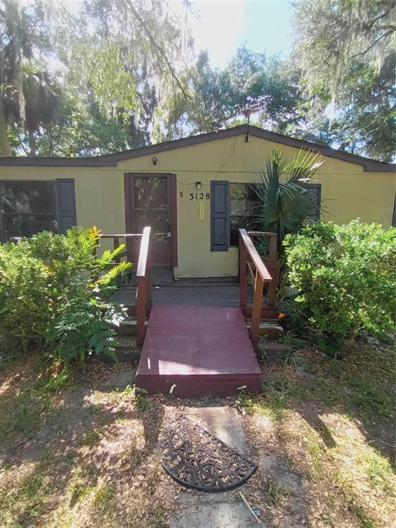 A single-story house with a wooden ramp leading to the front door and overgrown landscaping — 3128 CR 418, LAKE PANASOFFKEE, FL