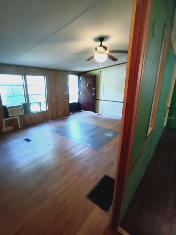 An interior view of a living room featuring wood-paneled walls, wood flooring, and a ceiling fan — 3128 CR 418, LAKE PANASOFFKEE, FL