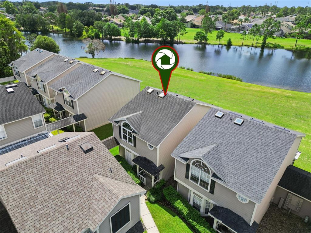 An aerial view shows several townhomes with gray shingled roofs situated near a large pond — 12122 BRUCETON WAY UNIT 103, ORLANDO, FL