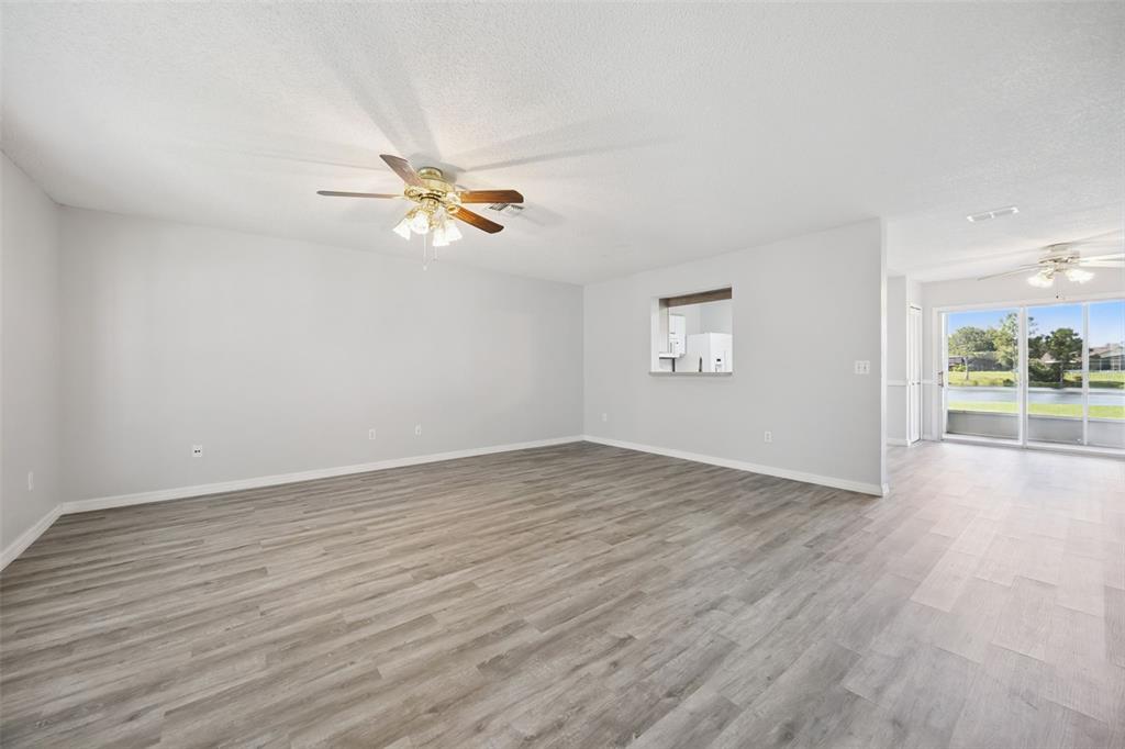An empty living room features light gray walls, wood-look flooring, a ceiling fan, and a pass-through — 12122 BRUCETON WAY UNIT 103, ORLANDO, FL