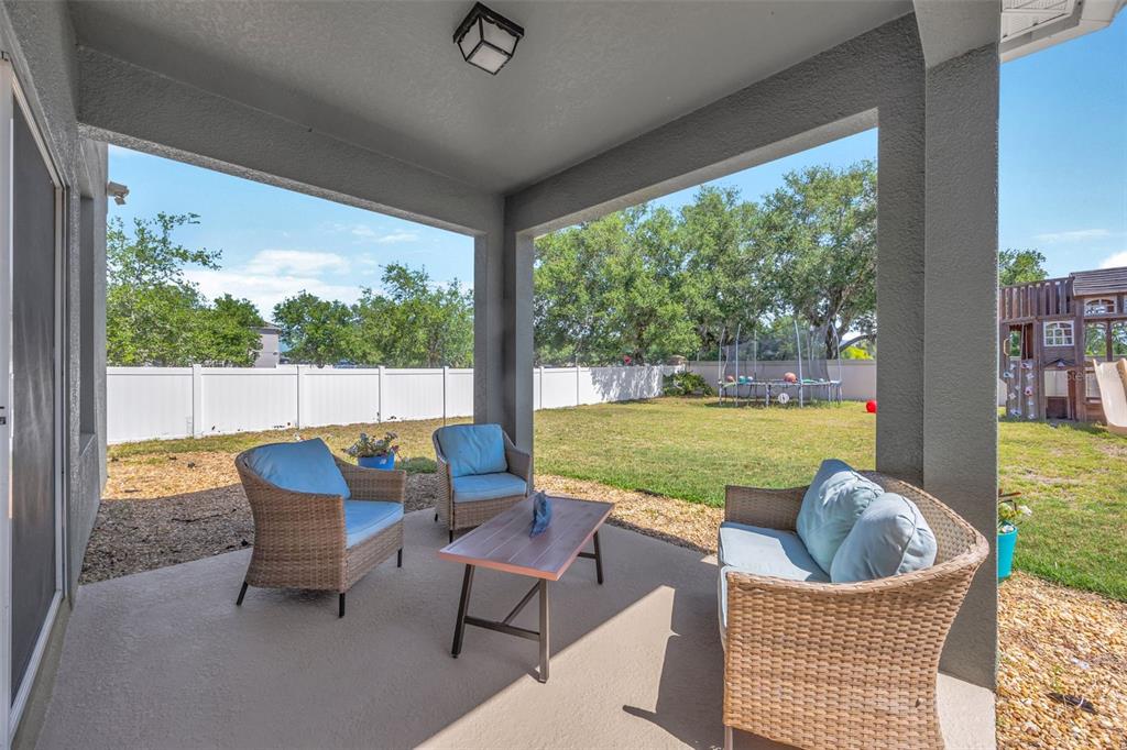 A covered concrete patio features wicker furniture and overlooks a fenced backyard with a playset — 5420 ANGELONIA TERRACE, LAND O LAKES, FL