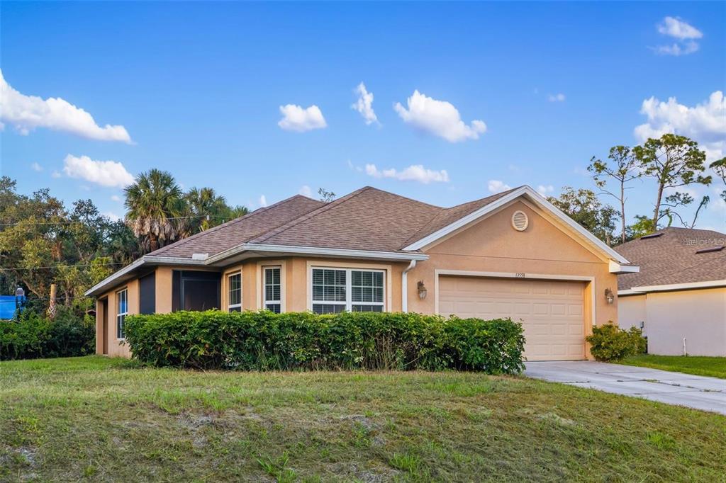 A single-story house with a tan stucco exterior, a two-car garage, and a front hedge — 13558 GOODRICH AVENUE, PORT CHARLOTTE, FL