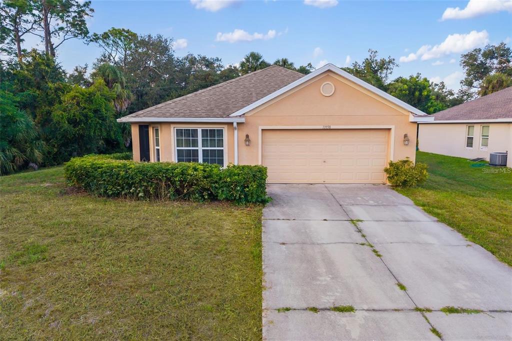 A single-story house with a beige stucco exterior, a two-car garage, and a concrete driveway — 13558 GOODRICH AVENUE, PORT CHARLOTTE, FL
