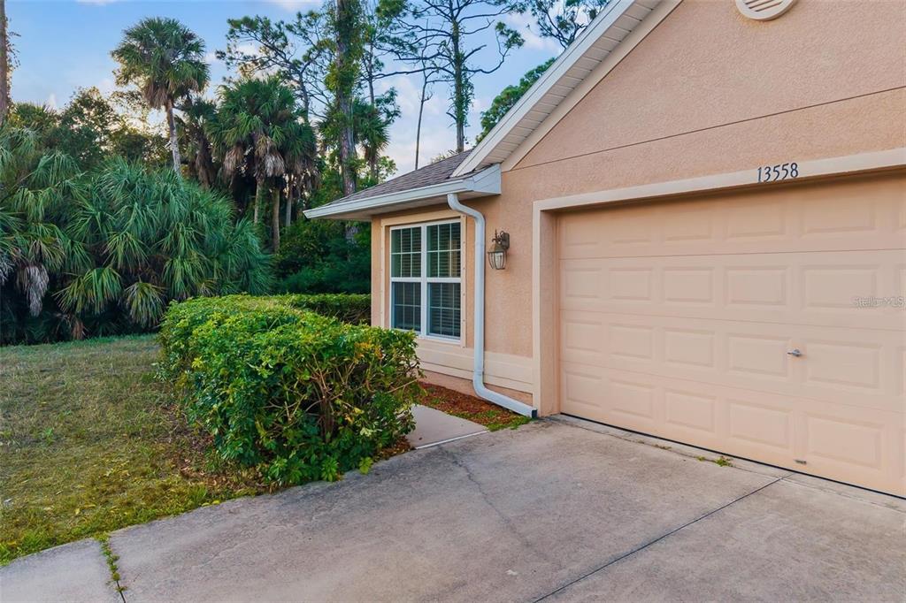 A beige house exterior features a garage door, a window, and a manicured hedge — 13558 GOODRICH AVENUE, PORT CHARLOTTE, FL